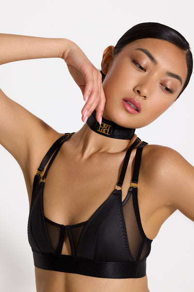 Bordelle Vero black wireless bralette. Opaque triangles cover sheer mesh bandeau with center cutout. Two adjustable satin elastic shoulder straps on each side. Front view on model in matching collar. 