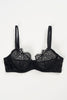 Else Monique black lace underwire bra, front view shown flat on plain white background. Bra features a three part cup with sheer black lining on bottom for added support and coverage. Scalloped eyelash lace trim at top of cup. Thin elastic shoulder straps. Lace underband.