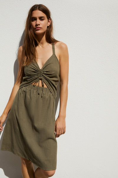 Else Ponza cotton dress in khaki green. The dress features a deep v neckline, halter style straps, a ruched front with tie closure, midriff cutout, elastic waistband, and an a-line knee length skirt. Shown on model, front view. 