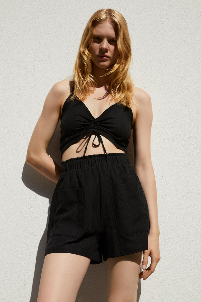 Else Ponza cotton crop top and matching shorts in black. The shorts feature a wide elastic waistband and front pockets. They have a high waist fit and mid thigh length. Shown on model, front view. 