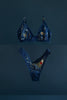 Eclipse Thong by Love & Swans. Dark blue mesh is embroidered and beaded with a sun and moon crossing paths, rays emitting from both and the latin words for "love conquers all." Shown flat with the matching Cygnus bralette.