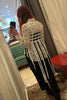 Ruban Noir black and white fringe top shown on model, back view. The top features a bandeau style woven bodice with long fringes of varying lengths reaching from low hip to knee length. Shown styled over white button up blouse with black print, black trousers and black pointy ankle boots.
