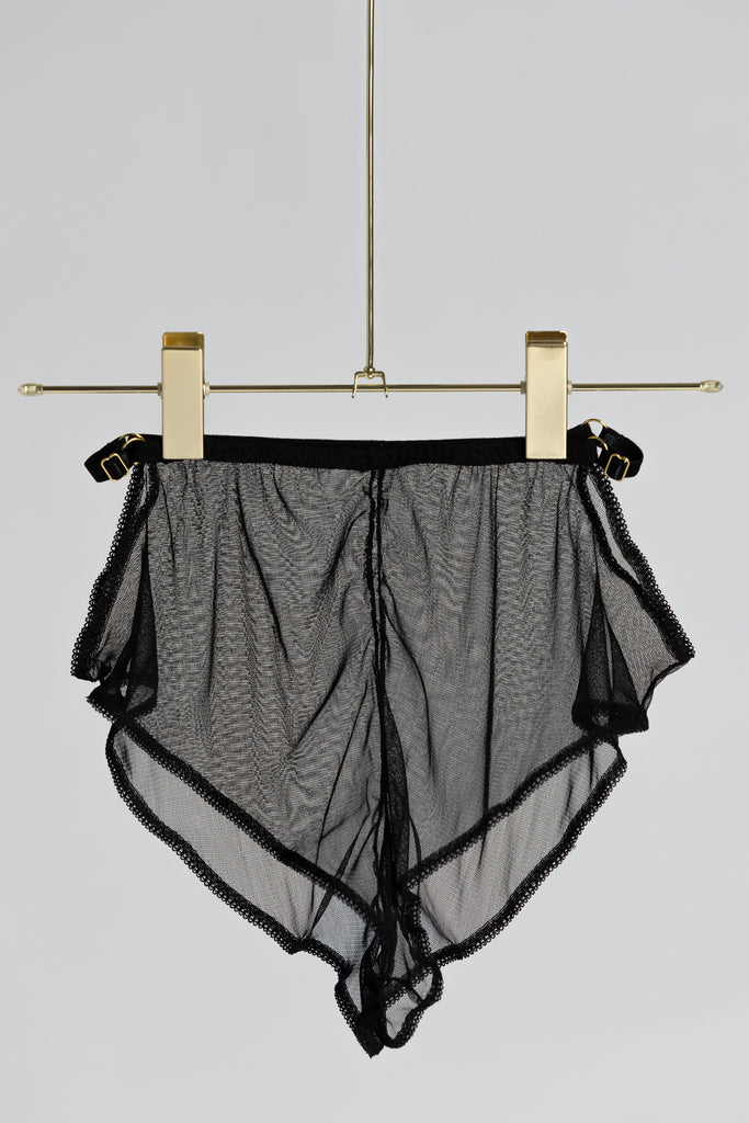 Sheer black Eartha Tap Pant by Adrina Dietra hanging from a gold hanger against a plain white background.