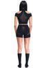DSTM Innsaei top in black, shown on model in matching shorts/brief. The Top features a mock nick, shoulder cutouts, short sleeve & cropped silhouette, and a sheer mesh panel in the center back. Back view.