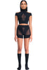 DSTM Innsaei top in black, shown on model in matching shorts/brief. The Top features a mock nick, shoulder cutouts, short sleeve & cropped silhouette, and a sheer mesh panel in the center front. Front view.