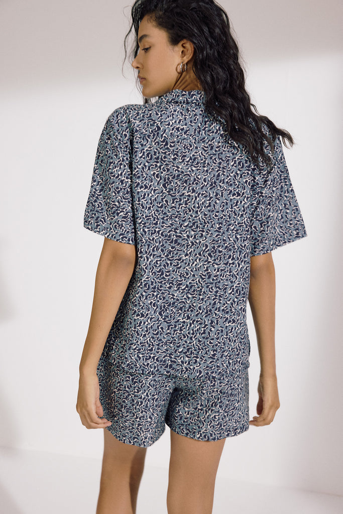 Naxos Camp Shirt by Else, shown on model with matching shorts. Shirt and shorts are light blue with an abstract dark blue and white print. Shown on model, back view