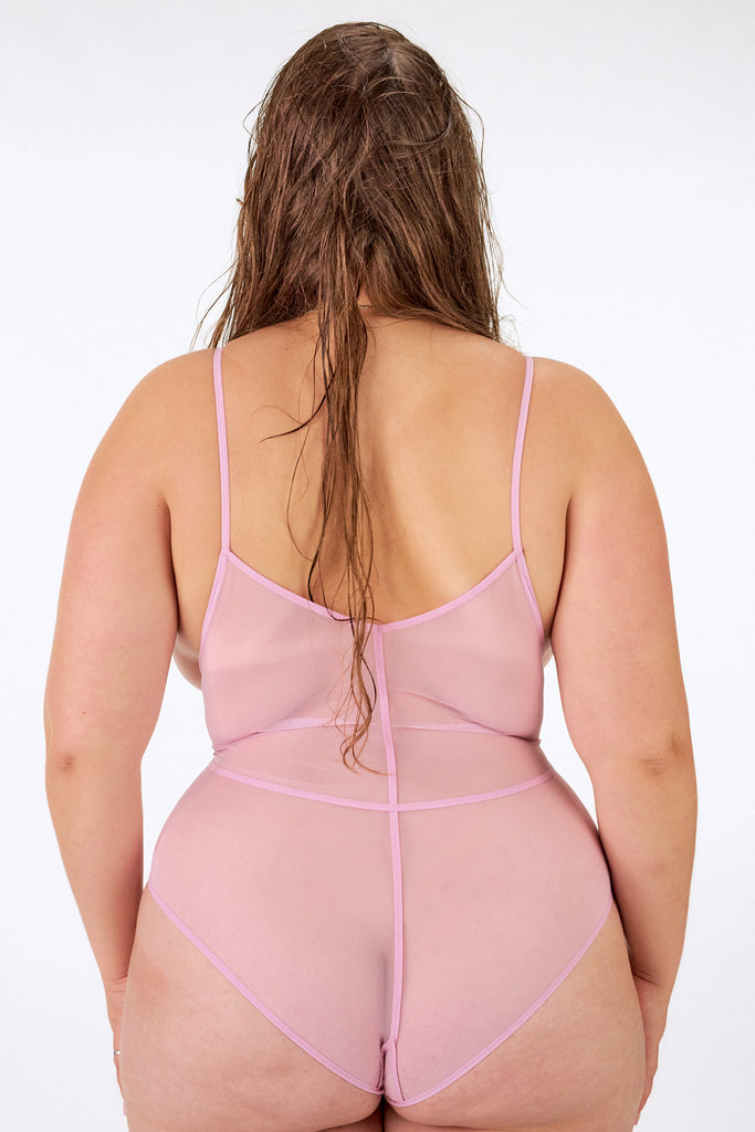Above bodysuit in pink rose by La Fille d'O. Back view on model shows the full coverage side with thin straps on the shoulders and sporty seams across the back.