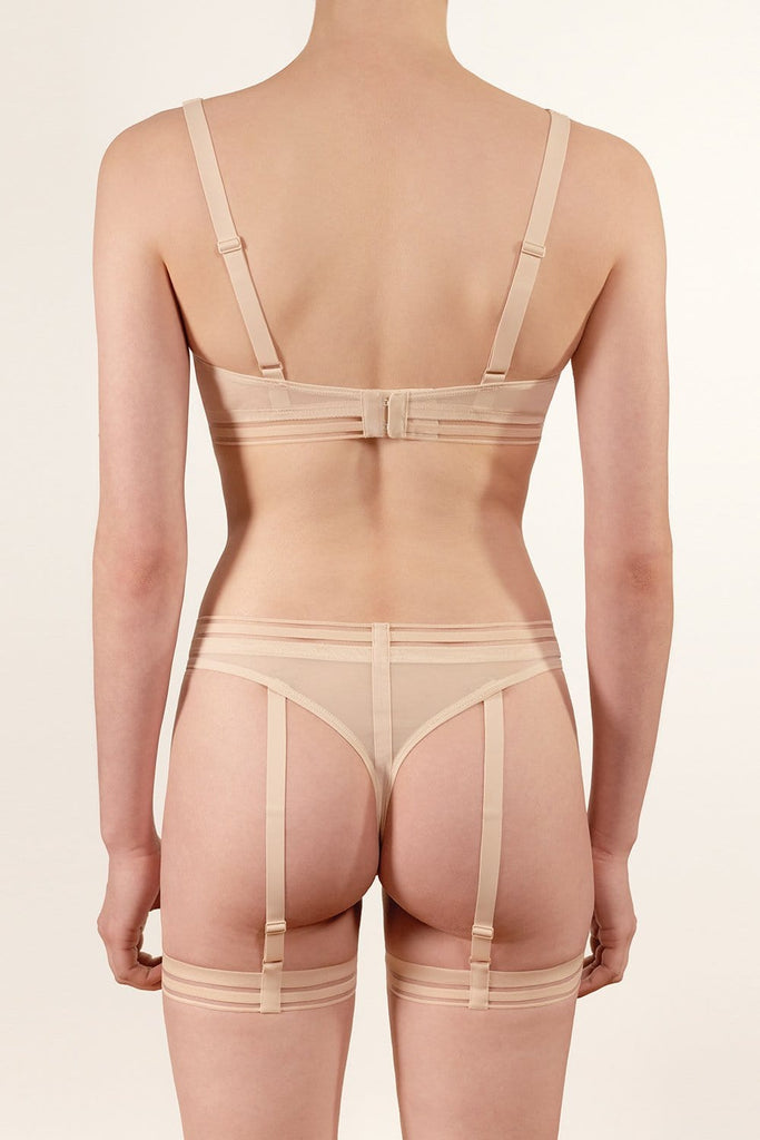 Opaak Lil leg strap garter in light beige (bleached sand), attached to matching Anou sheer mesh thong, back view, on model