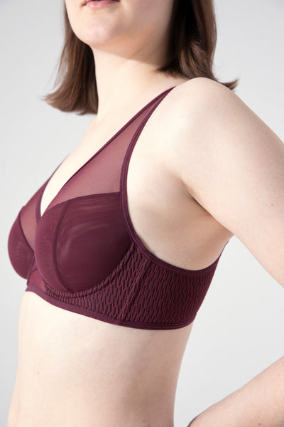 Opaak Magaly plunge underwire bra in Dawn (burgundy) mesh. Side view on model, showing the seamed cups that are opaque over the nipple and sheer on the chest. The underband also has a honeycomb textured fabric and side boning for added support.