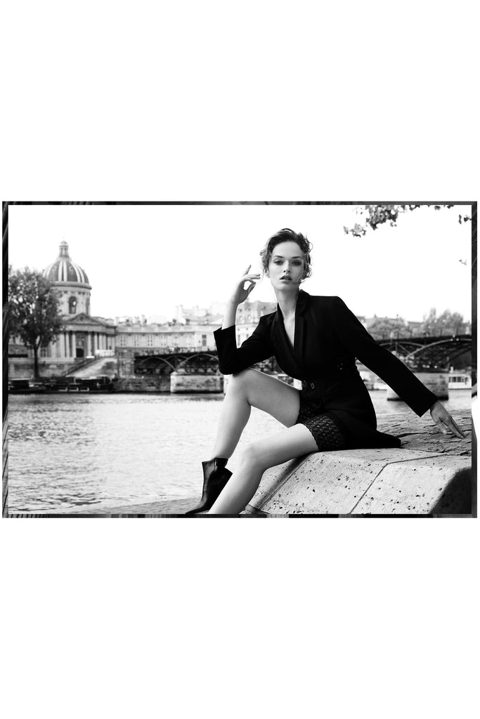 Seated model in front of river wearing Paloma Casile bike shorts, styled with black blazer and black boots.