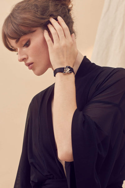 Paloma Casile's Sasha black wrist cuff with palladium closure. Shown on model in black robe who is lifting her hand to tuck her hair behind her ear.