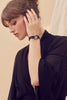 Paloma Casile's Sasha black wrist cuff with palladium closure. Shown on model in black robe who is lifting her hand to tuck her hair behind her ear.