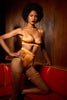 Amber orange petra soft bra by Studio Pia. Front view on the model shows a silky sheen in the fabric. The model is standing with one knee perched on a red upholstered booth with one hand on her hip, wearing matching high waist thong, garters, and choker.
