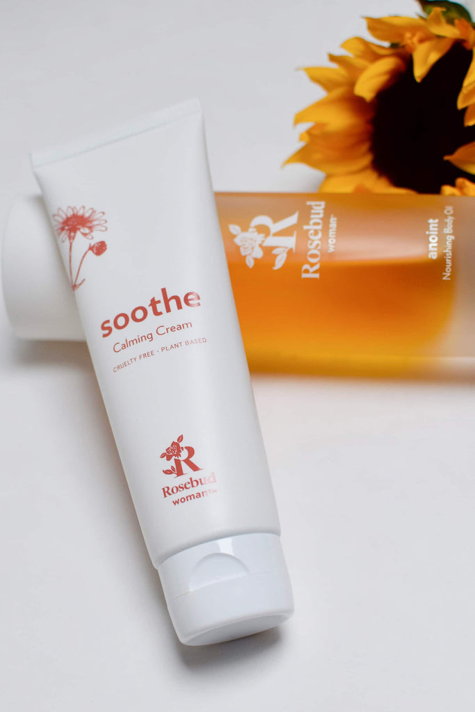 Rosebud Woman's Soothe Calming Cream white tube with pink label, and anoint oil and sunflower in the background