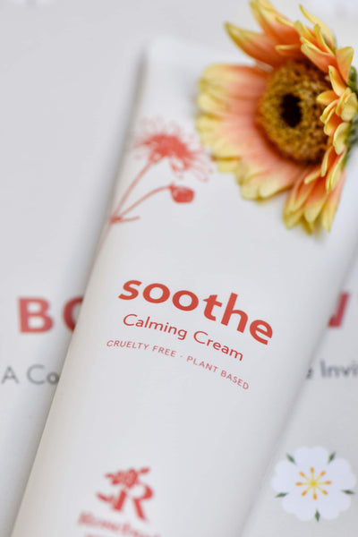 Close up of Rosebud Woman's Soothe Calming Cream label with yellow and orange flower in the background