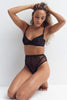 Sheer black crocodile mesh Cruz balcony bra with underwire by Taryn Winters. Front view on kneeling model wearing matching high waist thong. The model has both hand on her head running her hands through her hair. 