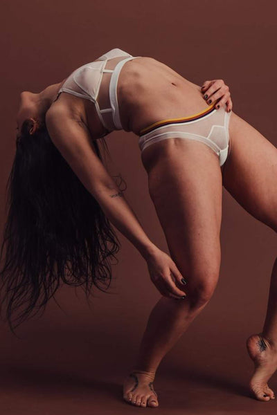 The Underargument sheer ivory mesh and striped elastic "Settling is not boring" thong, front/side view on model doing backbend in the matching longline bra