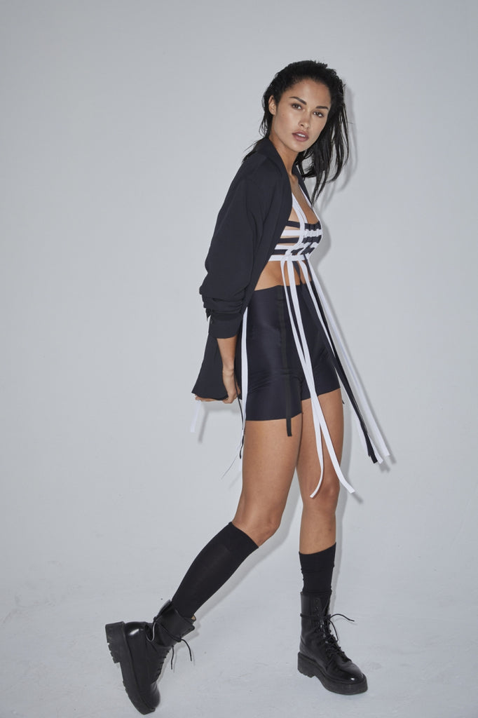 Ruban Noir black and white fringe bra top, shown on model, side view, with matching black blazer and bike shorts, and black knee socks and combat boots