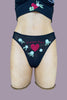 Only Hearts Aloha Vintage Thong in sheer black mesh with white and green floral embroidery surrounding and embroidered red heart and the words "lucky you." Front view on mannequin.