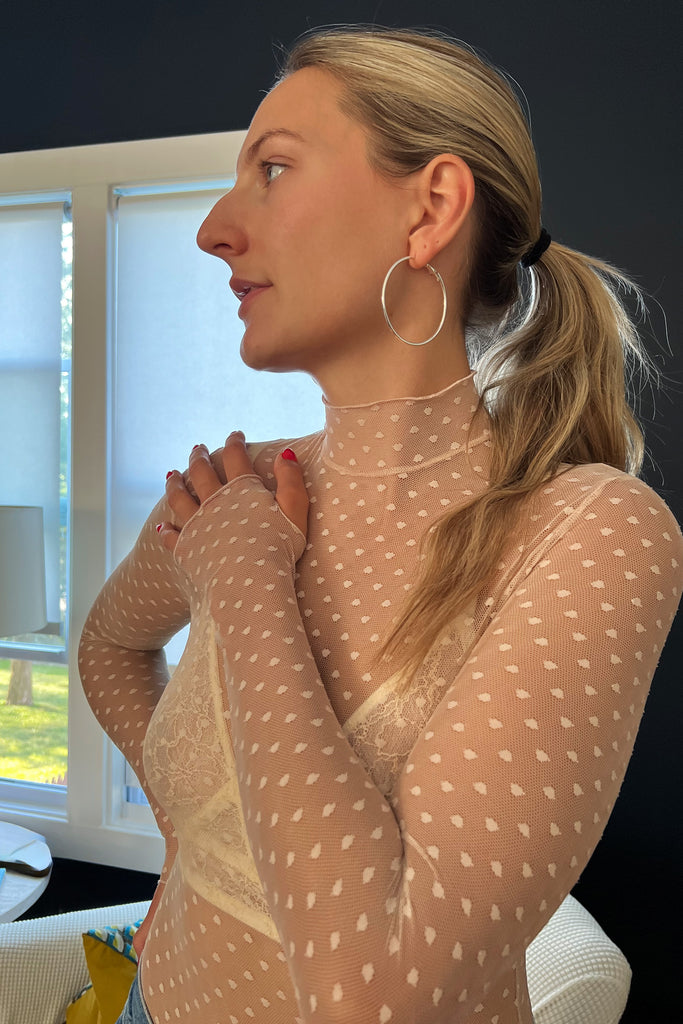 Close up of Only Hearts Coucou Lola long sleeve turtle neck bodysuit on model. Image shows ivory lace bralette underneath, thumbhole on sleeve, and sheer polka dot mesh of bodysuit.